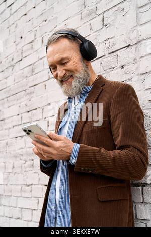 Ein älterer Mann sucht gerne sein Handy und genießt die lebhafte Atmosphäre der Stadt. Stockfoto