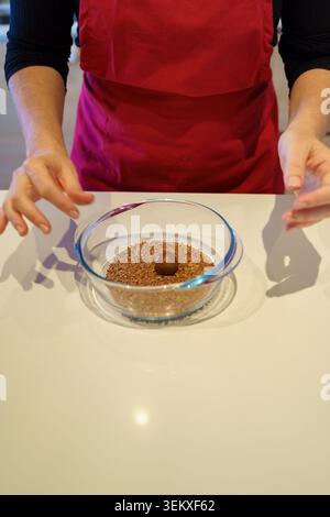 Frau in einer Schürze, die einen Schokoladentrüffel in einer Glasschale mit Streuseln zubereitet Stockfoto