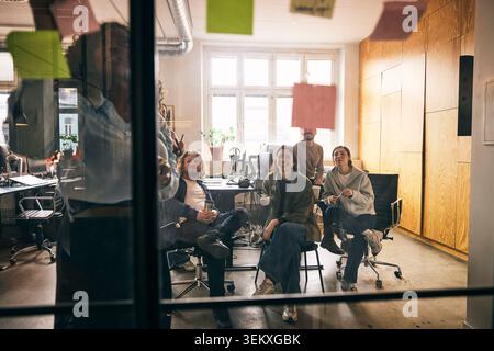 Gruppe von Geschäftsleuten, die in einem Meeting sitzen, während sie sich ansehen, wie Kollegen ihre Ideen im Büro durch Haftnotiz austauschen Stockfoto