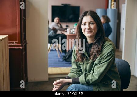 Porträt einer selbstbewussten lächelnden Geschäftsfrau, die mit Händen in der Technikzentrale sitzt Stockfoto