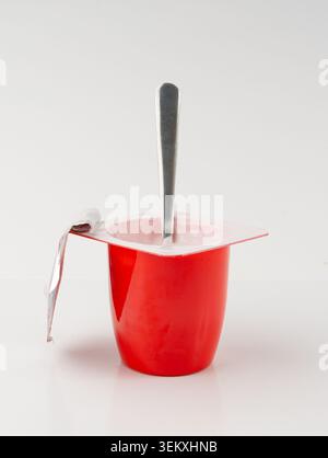 Joghurtbecher isoliert, rosafarbener Fruchtjoghurt im Plastiktopf, Milchpuddingbehälter mit Löffel, Milchkost kleines Paket auf weißem Hintergrund Stockfoto