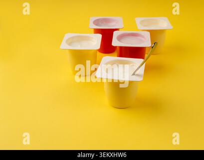 Joghurtbecher Set, rosafarbener und gelber Fruchtjoghurt in Plastiktöpfen, Milchpuddingbehälter mit Löffel, Milchkost kleines Paket auf farbigem Hintergrund Stockfoto