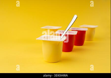 Joghurtbecher Set, rosafarbener und gelber Fruchtjoghurt in Plastiktöpfen, Milchpuddingbehälter mit Löffel, Milchkost kleines Paket auf farbigem Hintergrund Stockfoto