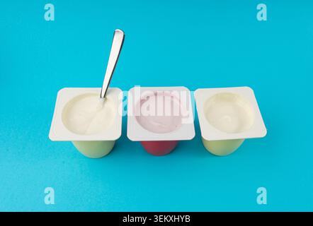 Joghurtbecher Set, rosafarbener und gelber Fruchtjoghurt in Plastiktöpfen, Milchpuddingbehälter mit Löffel, Milchkost kleines Paket auf farbigem Hintergrund Stockfoto
