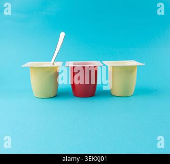 Joghurtbecher Set, rosafarbener und gelber Fruchtjoghurt in Plastiktöpfen, Milchpuddingbehälter mit Löffel, Milchkost kleines Paket auf farbigem Hintergrund Stockfoto