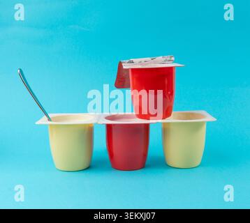 Joghurtbecher Set, rosafarbener und gelber Fruchtjoghurt in Plastiktöpfen, Milchpuddingbehälter mit Löffel, Milchkost kleines Paket auf farbigem Hintergrund Stockfoto