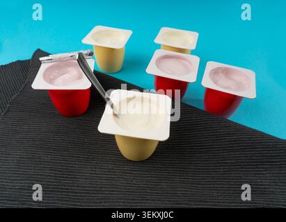 Joghurtbecher Set, rosafarbener und gelber Fruchtjoghurt in Plastiktöpfen, Milchpuddingbehälter mit Löffel, Milchkost kleines Paket auf farbigem Hintergrund Stockfoto