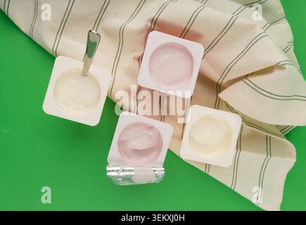 Joghurtbecher Set, rosafarbener und gelber Fruchtjoghurt in Plastiktöpfen, Milchpuddingbehälter mit Löffel, Milchkost kleines Paket auf farbigem Hintergrund Stockfoto