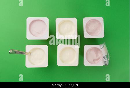 Joghurtbecher Set, rosafarbener und gelber Fruchtjoghurt in Plastiktöpfen, Milchpuddingbehälter mit Löffel, Milchkost kleines Paket auf farbigem Hintergrund Stockfoto