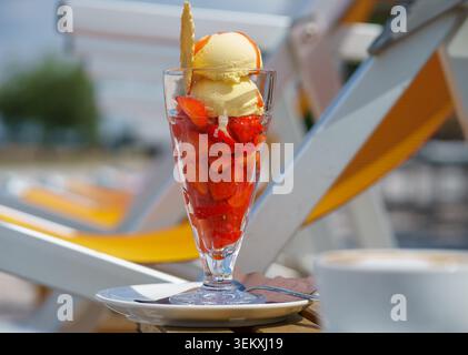Frisches Erdbeerdessert mit Vanilleeis im Glas, serviert im Freien auf der sonnigen Terrasse, Sommervergnügen, süßes Essenskonzept und Entspannung. Stockfoto