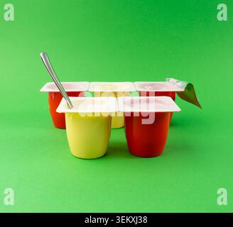 Joghurtbecher Set, rosafarbener und gelber Fruchtjoghurt in Plastiktöpfen, Milchpuddingbehälter mit Löffel, Milchkost kleines Paket auf farbigem Hintergrund Stockfoto