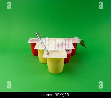 Joghurtbecher Set, rosafarbener und gelber Fruchtjoghurt in Plastiktöpfen, Milchpuddingbehälter mit Löffel, Milchkost kleines Paket auf farbigem Hintergrund Stockfoto
