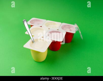 Joghurtbecher Set, rosafarbener und gelber Fruchtjoghurt in Plastiktöpfen, Milchpuddingbehälter mit Löffel, Milchkost kleines Paket auf farbigem Hintergrund Stockfoto