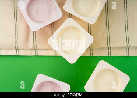 Joghurtbecher Set, rosafarbener und gelber Fruchtjoghurt in Plastiktöpfen, Milchpuddingbehälter mit Löffel, Milchkost kleines Paket auf farbigem Hintergrund Stockfoto