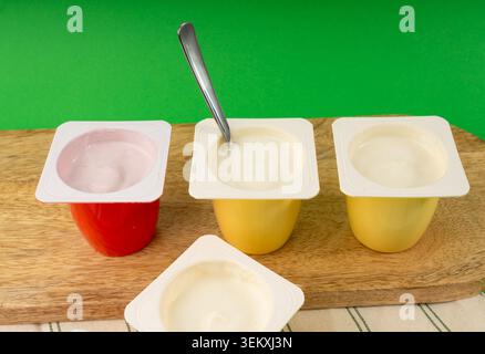 Joghurtbecher Set, rosafarbener und gelber Fruchtjoghurt in Plastiktöpfen, Milchpuddingbehälter mit Löffel, Milchkost kleines Paket auf farbigem Hintergrund Stockfoto