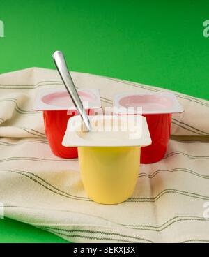 Joghurtbecher Set, rosafarbener und gelber Fruchtjoghurt in Plastiktöpfen, Milchpuddingbehälter mit Löffel, Milchkost kleines Paket auf farbigem Hintergrund Stockfoto