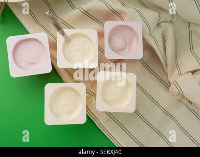 Joghurtbecher Set, rosafarbener und gelber Fruchtjoghurt in Plastiktöpfen, Milchpuddingbehälter mit Löffel, Milchkost kleines Paket auf farbigem Hintergrund Stockfoto