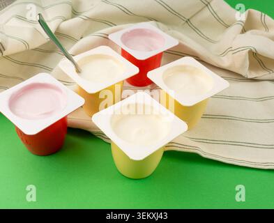 Joghurtbecher Set, rosafarbener und gelber Fruchtjoghurt in Plastiktöpfen, Milchpuddingbehälter mit Löffel, Milchkost kleines Paket auf farbigem Hintergrund Stockfoto