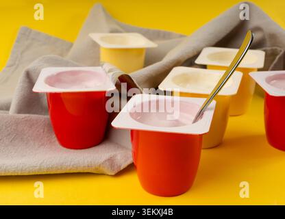 Joghurtbecher Set, rosafarbener und gelber Fruchtjoghurt in Plastiktöpfen, Milchpuddingbehälter mit Löffel, Milchkost kleines Paket auf farbigem Hintergrund Stockfoto