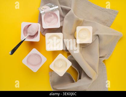 Joghurtbecher Set, rosafarbener und gelber Fruchtjoghurt in Plastiktöpfen, Milchpuddingbehälter mit Löffel, Milchkost kleines Paket auf farbigem Hintergrund Stockfoto
