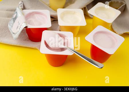 Joghurtbecher Set, rosafarbener und gelber Fruchtjoghurt in Plastiktöpfen, Milchpuddingbehälter mit Löffel, Milchkost kleines Paket auf farbigem Hintergrund Stockfoto
