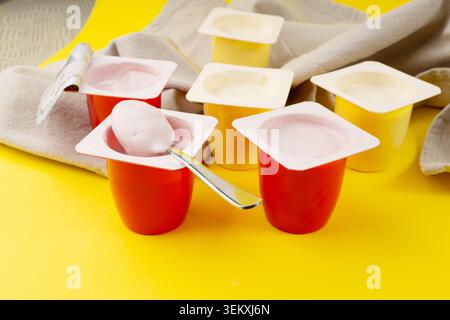 Joghurtbecher Set, rosafarbener und gelber Fruchtjoghurt in Plastiktöpfen, Milchpuddingbehälter mit Löffel, Milchkost kleines Paket auf farbigem Hintergrund Stockfoto