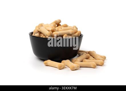 Hundekekse in schwarzer Schüssel isoliert, weiche knusprige Haustierspezialitäten, aromatisierter kleiner Eckkeks, Kekse in Knochenform, Welpenübungsfutter auf weißem Hintergrund Stockfoto