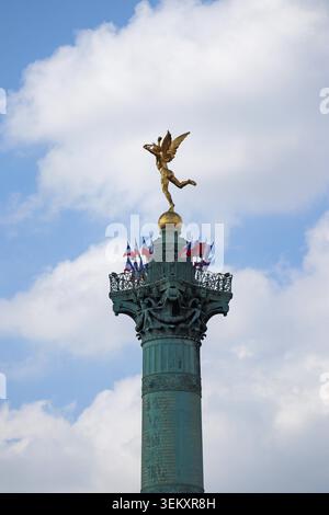 Paris, Frankreich - 7. Mai 2022: Juli-Säule mit goldener geflügelter Statue und französischen Fahnen am Place de la Bastille vor blauem Himmel Stockfoto