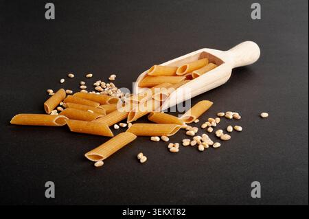 Rohe braune Nudeln, Vollkorn-Penne-Stapel in Scoop, trockene Vollkornnudeln, rohe Dinkel-Makkaroni, gesunde italienische Lebensmittel, Bio-Mahlzeit, Weizen-Pasta auf Bla Stockfoto