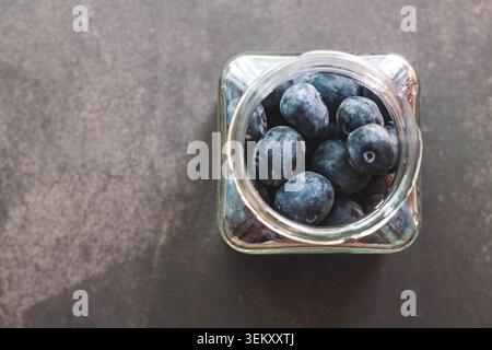 Frische Blaubeeren im Glasglas von oben auf dunklem Hintergrund Stockfoto