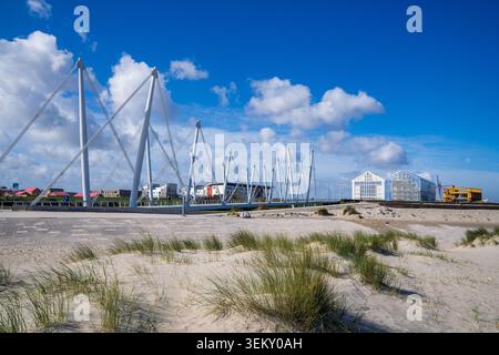 Blick auf die moderne Fußgängerbrücke mit hohen weißen Masten und Stahlseilen in Dünkirchen. Sanddünen mit grünen Grasbüscheln dominieren den Vordergrund Stockfoto