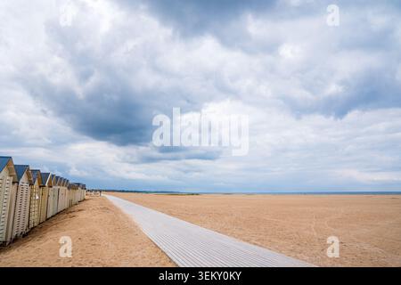Ein Blick auf den hölzernen Wanderweg am breiten Sandstrand von Lion-sur-Mer, Normandie. Traditionelle Strandhütten stehen auf der linken Seite, un Stockfoto
