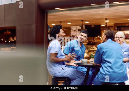Männliches und weibliches medizinisches Personal, das sich während der Kaffeepause in der Cafeteria des Krankenhauses unterhalten Stockfoto