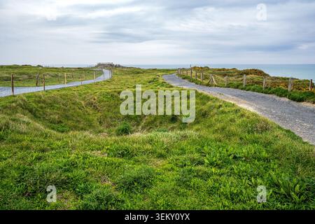 Großer Blick auf die historische Stätte Pointe du hoc in der Normandie. Zwei Fußgängerwege mit Holzzäunen winden sich über die grünen Küstenklippen scarr Stockfoto