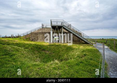 Vorderansicht eines massiven Betonbunkers bei Pointe du hoc. Das Gebäude verfügt über eine breite Metalltreppe und eine Aussichtsplattform für Touristen, flankiert von Stockfoto