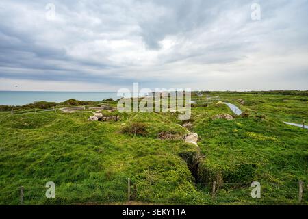 Weiter Blick auf Pointe du hoc mit Blick auf das Meer. Die grasbewachsene Kraterlandschaft bietet Betonbunkerruinen, Gräben und lange graue Wanderwege für VI Stockfoto