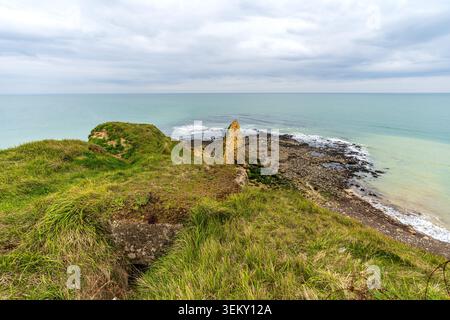 Panoramablick von den grasbewachsenen Klippen von Pointe du hoc. Darunter befindet sich ein Kiesstrand, ein spitzer Seestapel im Wasser und der weite Meereshorizont Stockfoto