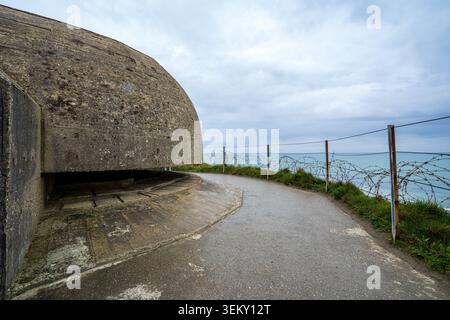 Winkelansicht der Betonkuppel des Beobachtungsbunkers bei Pointe du hoc. Daneben verläuft ein nasser Fußgängerweg entlang eines Stacheldrahtzaunes mit Blick auf die Stockfoto