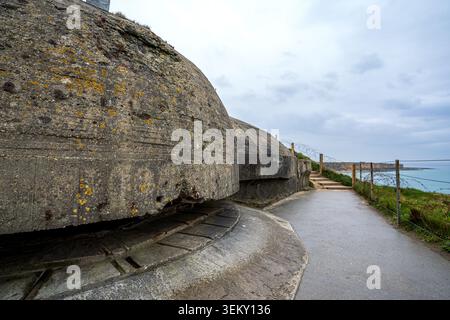 Winkelansicht der Betonkuppel des Beobachtungsbunkers bei Pointe du hoc. Daneben verläuft ein nasser Fußgängerweg entlang eines Stacheldrahtzaunes mit Blick auf die Stockfoto