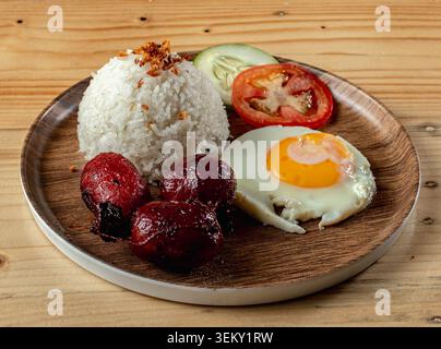 Nahaufnahme eines Chorizo-Frühstücks mit gebratenem Reis, Ei, Tomatenscheiben und Gurke auf einem Holzteller. Stockfoto