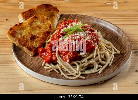 Nahaufnahme von käsigen Spaghetti mit geröstetem Brot auf einem Holzteller. Stockfoto