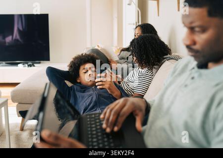 Kinder verbringen Freizeit mit Smartphones, während sie sich mit der Familie zu Hause auf dem Sofa entspannen Stockfoto