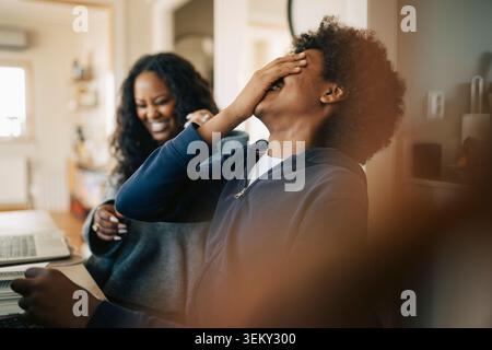 Glücklicher Junge lacht, während er zu Hause neben der Mutter sitzt Stockfoto