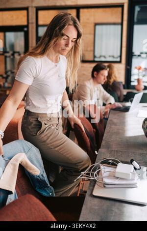 Geschäftsfrau mit blonden Haaren, die auf einem Stuhl am gemeinsamen Schreibtisch im Coworking-Bereich sitzt Stockfoto