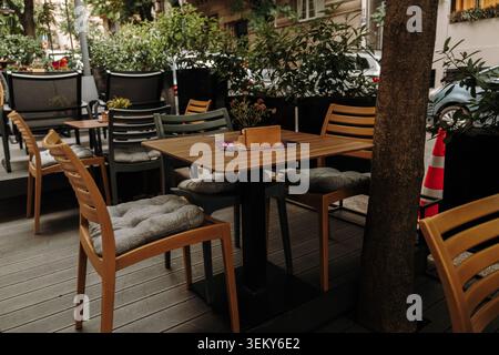 Moderne Restaurantterrasse mit Holztischen und Stühlen, umgeben von Grünpflanzen. Konzept für Gastgewerbe und urbanen Lebensstil. Stockfoto