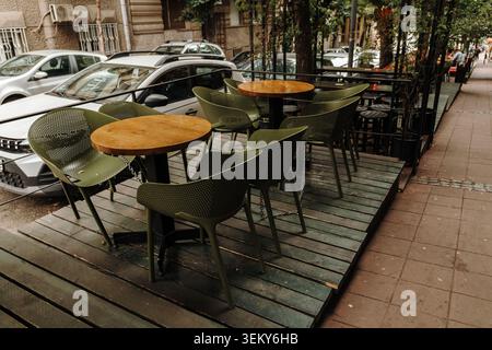 Leere Außenterrasse eines Cafés mit runden Holztischen und modernen Stühlen. Gastronomie- und Freizeitkonzept in einer städtischen Umgebung. Stockfoto