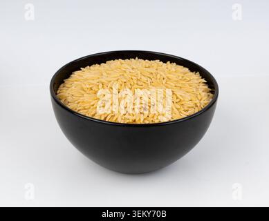 Roher Orzo-Nudelhaufen in Schüssel isoliert. Risoni-Pasta in Form eines großen Reiskörns, griechischer Kritharaki-Stapel auf weißem Hintergrund Stockfoto