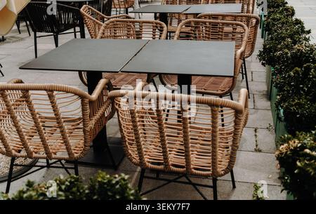 Gewebte Stühle und Tische sind in einem modernen Essbereich im Freien angeordnet. Gastfreundschaft und Restaurantkonzept. Stockfoto