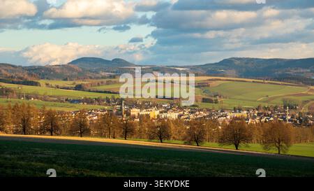 Stadt eingebettet in ein Tal mit sanften grünen Feldern und fernen Hügeln unter einem bewölkten Himmel Stockfoto