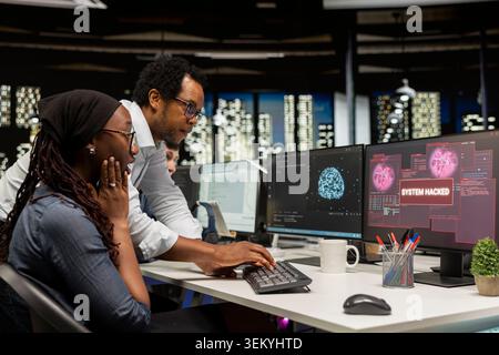 Ein junger unerfahrener Programmierer im Büro bittet den Teamleiter um Hilfe, um Hackerversuche im Unternehmensnetzwerk zu beheben. Praktikant, der von einem Manager unterstützt wird, um Warnungen wegen unbefugten Zugriffs zu untersuchen Stockfoto